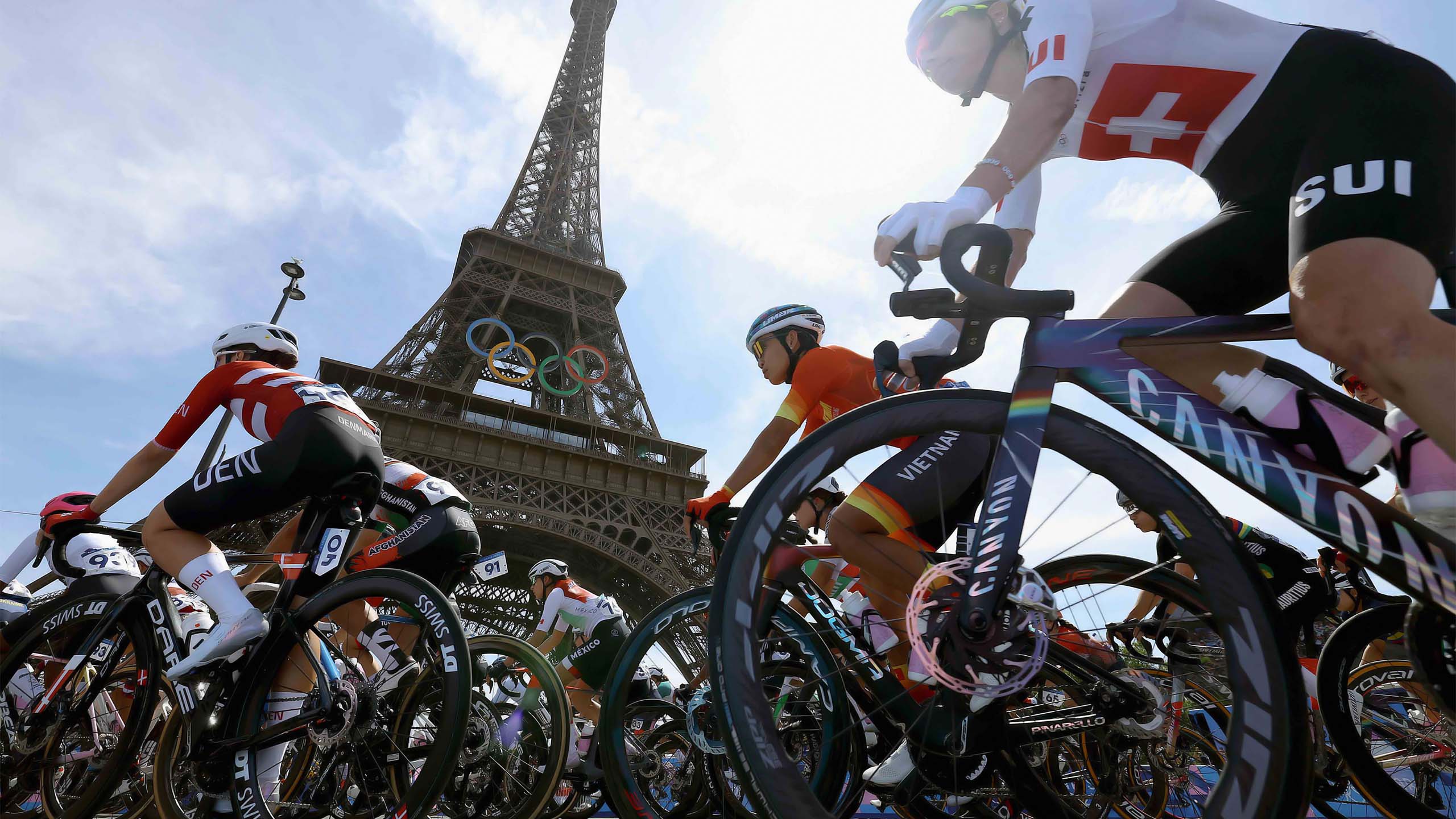 Cyclists from multiple nations race past the Eiffel Tower during the Paris 2024 Olympic Games, with the Olympic rings displayed beneath the landmark.