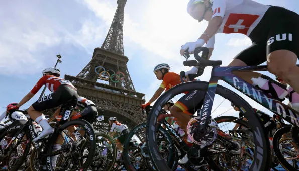 Cyclists from multiple nations race past the Eiffel Tower during the Paris 2024 Olympic Games, with the Olympic rings displayed beneath the landmark.